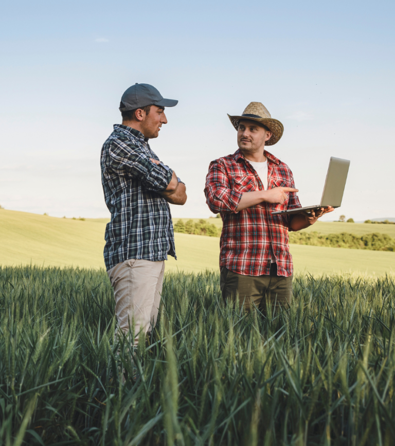 Zwei Landwirte sprechen auf einem Feld, während einer einen Laptop hält.